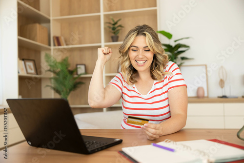 A woman jubilantly raises her fist in excitement while shopping online, capturing a moment of joy and accomplishment.