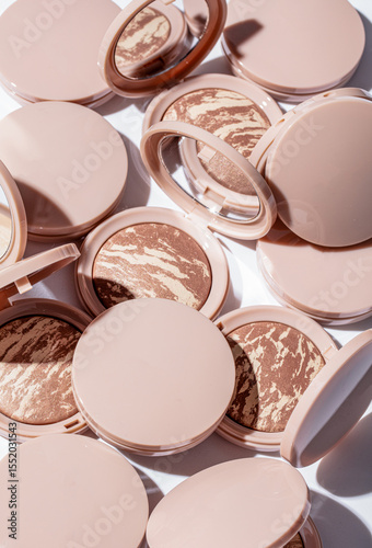 Various compact powders with unique marble patterns are spread across a flat surface, reflecting light from surrounding mirrors, highlighting their diverse textures and colors.