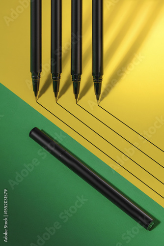 Black pens and a marker are meticulously arranged on a vibrant yellow and green background, creating a visually appealing layout that inspires creativity and design.