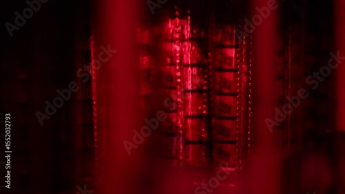 Dramatic close-up of a vintage film reel rotating and unwinding, bathed in striking red light. Perfect for cinematic, nostalgic, or artistic projects, evoking classic movie themes and atmosphere.
