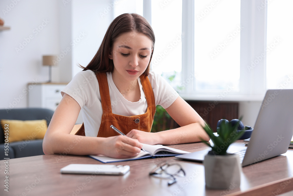 Teenage girl doing homework at table indoors Teenage girl doing homework at table indoors