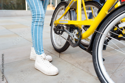 Urban cyclist prepares for a ride on a bright yellow bike on a sunny day in a modern city setting surrounded by pavement and buildings
