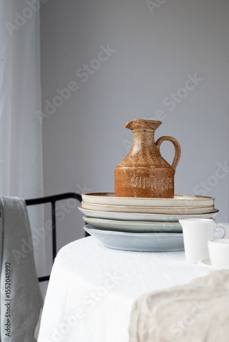 Vintage brown ceramic pitcher on stacked plates, Scandinavian kitchen style, rustic minimalism, cozy home deco