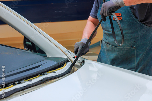 Technician works on replacing windshield seal in bright garage during replacement damaged windshield