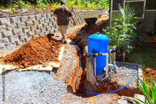 Homeowner works on installing water well pump system near trench in thoughtfully arranged outdoor space.