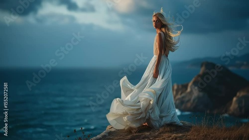Woman in a flowing white dress stands on a cliff overlooking the ocean, wind in her hair and dress, with dramatic clouds and waves in the background.
