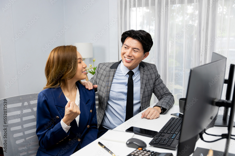 Obraz premium Successful smiling Asian business partners raising fist up together in profitable project job in stock exchange database on pc wearing formal suit at modern home office at side view image. Infobahn.