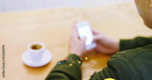 Adult male tapping smartphone checking social media floating reaction emojis over table with cup
