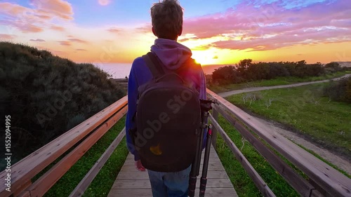 A teenager with a backpack goes to the edge of a cliff at Ponta de Piedad to see the most beautiful sunset in the ocean, Portugal