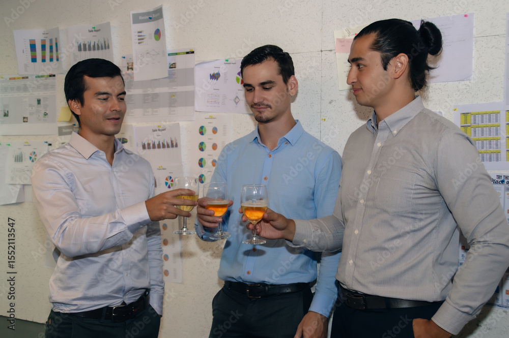 © S photographer - Three professionals celebrating success with drinks in a modern office environment, showcasing teamwork.
