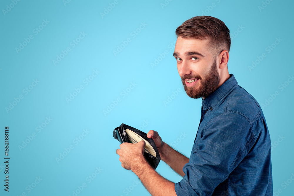 Funky Caucasian guy holding full wallet with money on blue studio background. Wealthy young man with purse of dollars, achieving financial success, receiving raise of salary or profit Funky Caucasian guy holding full wallet with money on blue studio background. Wealthy young man with purse of dollars, achieving financial success, receiving raise of salary or profit
