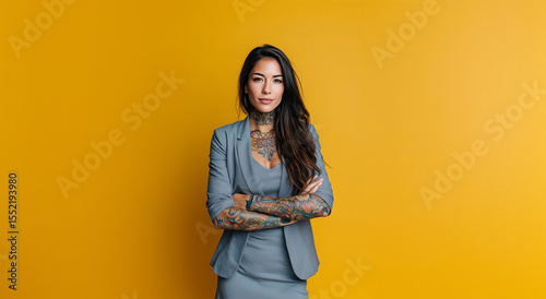 Confident woman with tattoos poses in business attire against vibrant yellow background showcasing her unique style and professionalism