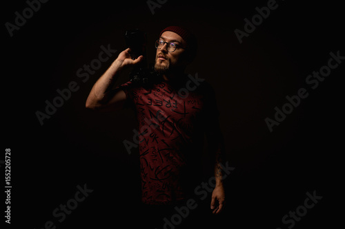 Moody portrait of a stylish photographer in beanie and glasses holding a camera on shoulder. Artistic low-key lighting highlights creative expression and focus