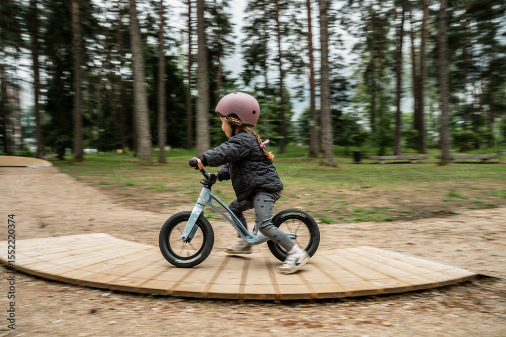 Fototapeta premium little child riding balance bike on wooden curved track in forest park, outdoor activity for toddlers, early cycling skill development, kids sport training, natural playground fun, safety helmet gear