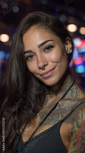 Smiling woman with tattoos and long dark hair captured in an urban setting with colorful bokeh lights, showcasing her unique style and confident demeanor