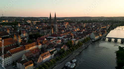 Regensburg at sunset captured from above, featuring the iconic Stone Bridge over the Danube River and the majestic twin towers of St. Peter's Cathedral glowing in warm evening light