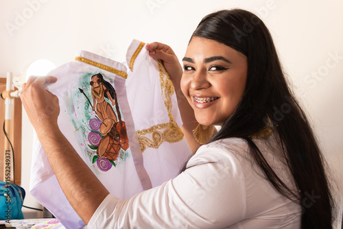 A Colombian woman is smiling while holding a white shirt and looking at the camera. Concept of creativity and businesswomen