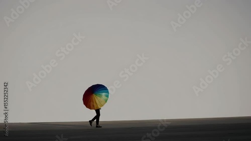 Silhouetted figure holding a vibrant rainbow umbrella, creating a stark contrast against a bright minimalist background, symbolizing individuality and hope