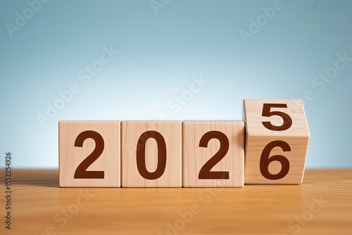 Wooden blocks display the year twenty twenty five transitioning to twenty twenty six on a wooden surface with a soft blue background