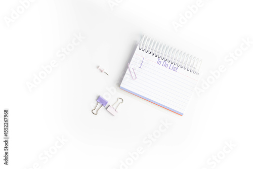 Purple To do list with 1, 2, and 3 listed on lined paper in a notebook with paper clips and push pins on white background,