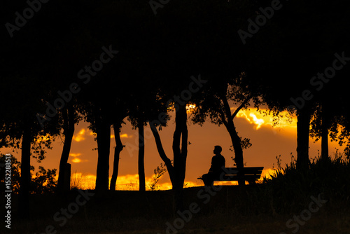 Silueta de hombre sentado en un banco, viendo el atardecer