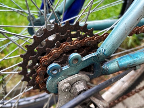 Close-up of a rusty bicycle chain and gear mechanism attached to a weathered blue frame with metal spokes in focus