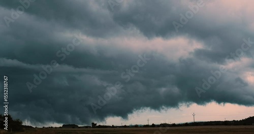 Timelapse of scary massive dark blue storm clouds gathering dramatically in the sky above a field and having wisps of condensation reaching to the ground reminding of little tornadoes