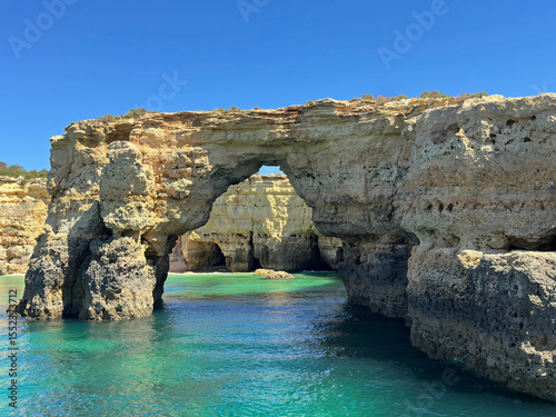The Arco de Albandeira rock arch and sea caves are shown along the Algarve region or Portugal, near the town of Porches, during a sunny day.