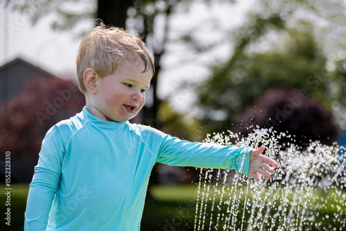 Happy little boy putting his hand in a spray of water