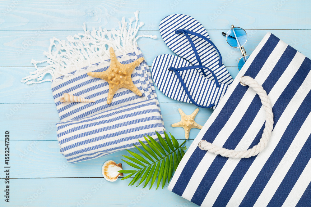 Obraz premium Blue beach bag with summer accessories on wooden background, top view