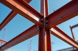Close-up of steel structure construction with clear blue sky background. Red metal beams join with bolts. Modern architecture framework industrial design.
