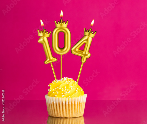Yellow birthday cupcake with a number 104 candle - Birthday card on a pink background