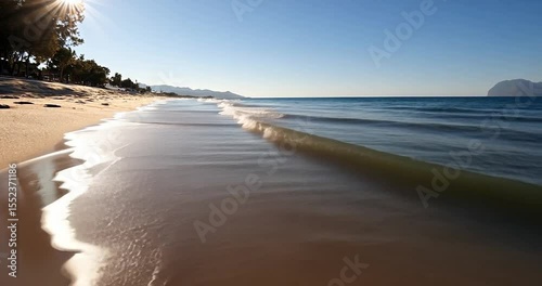 Video of tranquil sunlit beach scene gentle waves lapping shore clear blue sky sunshine and soft white foam perfect day
