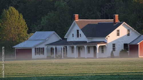 Picturesque midwestern farmhouse stands serene in the morning light, its white siding gleaming as a gentle mist hangs over the lush green meadow, creating a tranquil rural scene