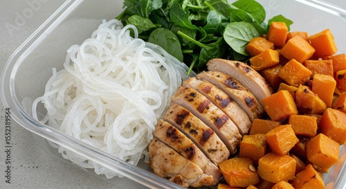 Healthy Meal Prep with Grilled Chicken, Butternut Squash, Rice Noodles, and Fresh Spinach in a Transparent Container