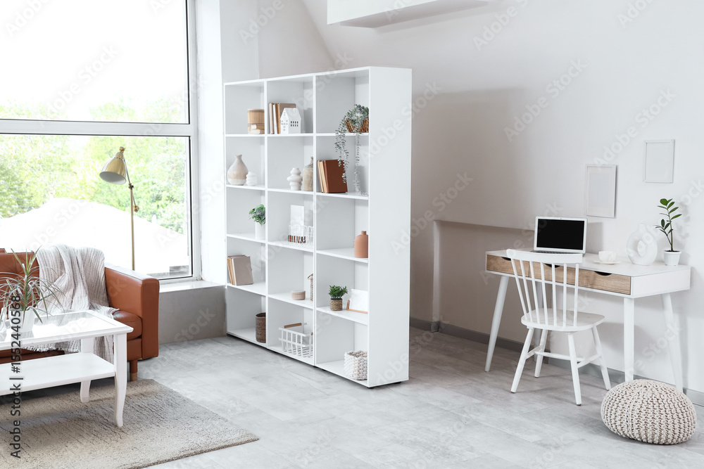 Fototapeta premium Interior of light living room with shelf unit, sofa and workplace