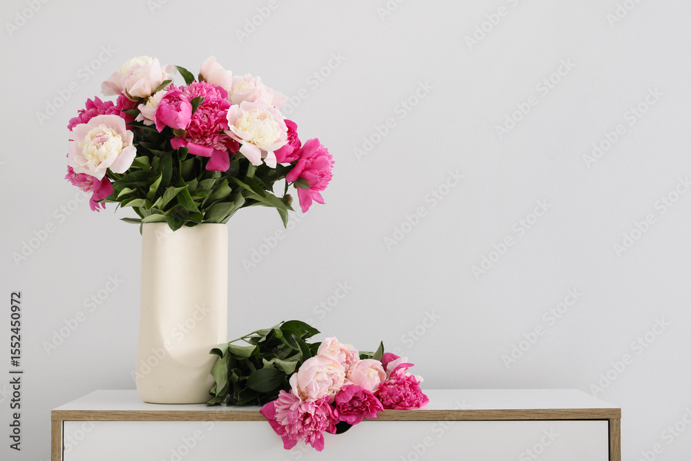 Fototapeta premium Vase with beautiful peony flowers on chest of drawers near white wall in interior of room, closeup