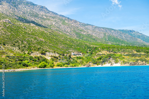 South of Ikaria island, Greece landscape of Livadi beach at Greek mountains cliff and white clouds in blue sky at Icarian Mediterranean sea water