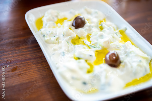 Tzatziki traditional Greek yogurt sauce homemade food on Ikaria island of Aegean Greece macro closeup in olive oil herbs on wooden table