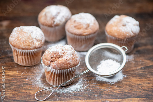 Delicious cupcakes sprinkled with powdered sugar stand on a wooden table