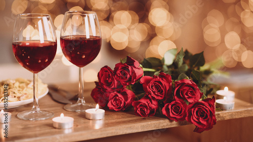 Romantic Dinner. Bouquet of flowers lying on the table, selective focus on bunch of roses, two glasses of red wine and candles on the wooden desk. Date concept, blurred background, banner, copy space