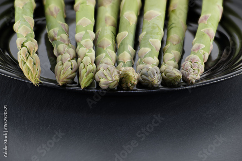 Green asparagus spears arranged on a sleek black plate, ready to be prepared for a meal.