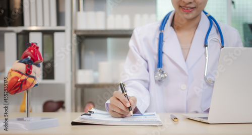 Photography A young Asian female doctor works alone at her desk, reviewing cardiovascular patient records
