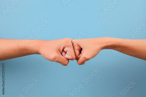 Close Up Of Two Fists Bumping Against Each Other Isolated On Blue Background