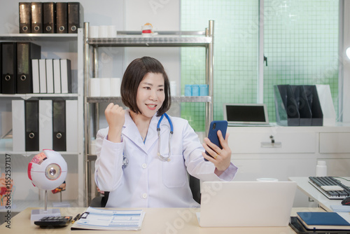 A middle-aged Asian female doctor holds an eye model at her desk, explaining eye anatomy and vision problems.She educates patients or, demonstrating knowledge as an optometrist or medical instructor