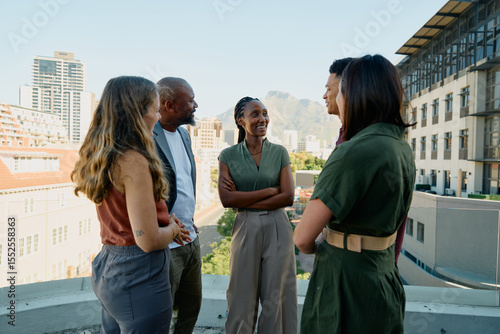 Smiling black businesswoman talking with colleagues on rooftop terrace during daytime