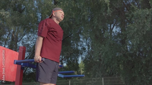A 62 year old man is training on a sports ground. Push-ups on the bars.