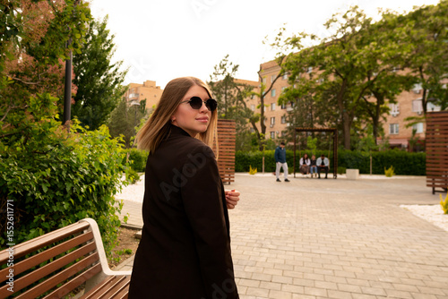Stylish young woman walking outdoors in urban park daytime.