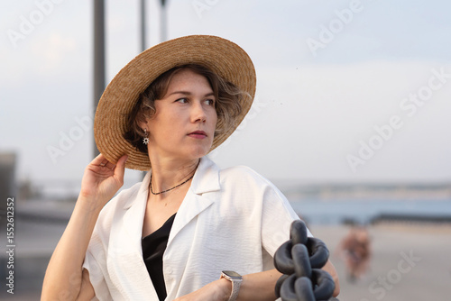 Thoughtful woman in straw hat seated near seaside promenade.