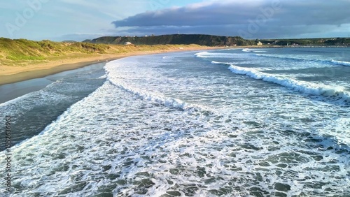 Experience the soothing sound of tranquil ocean waves gently lapping against a golden sandy beach beneath a cloudy sky